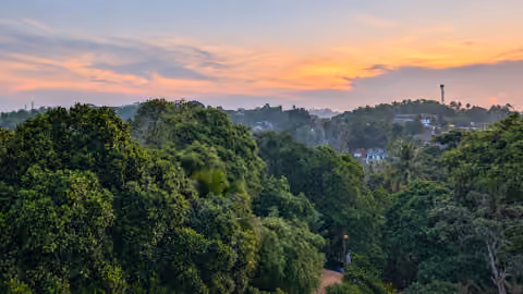 Dawn sky in pink and orange over layers of green treetops and hills in Galle, seen from a sixth-floor balcony at Greenview Apartment